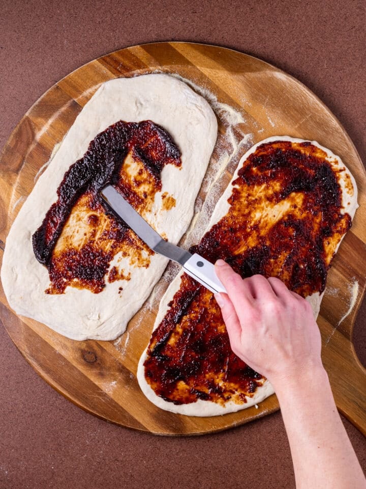 hand spreading fig jam on pizza dough