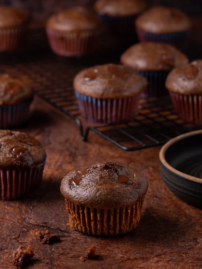 Double chocolate oat muffins cooling on a wire rack with melted chocolate pieces throughout.