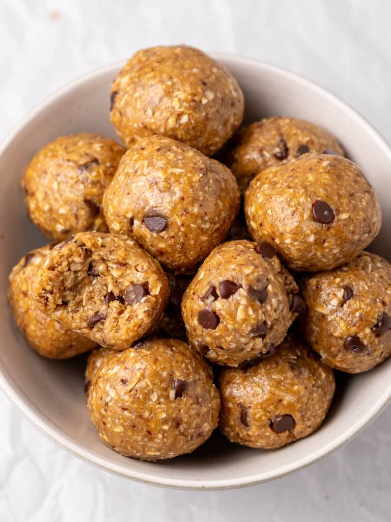 Peanut butter oatmeal balls with mini chocolate chips piled in a white bowl, with one bitten into.