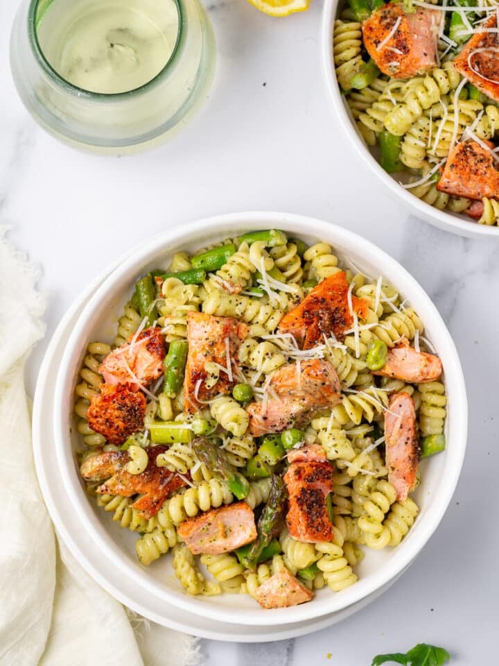 white bowl with pesto pasta and salmon, glass of wine