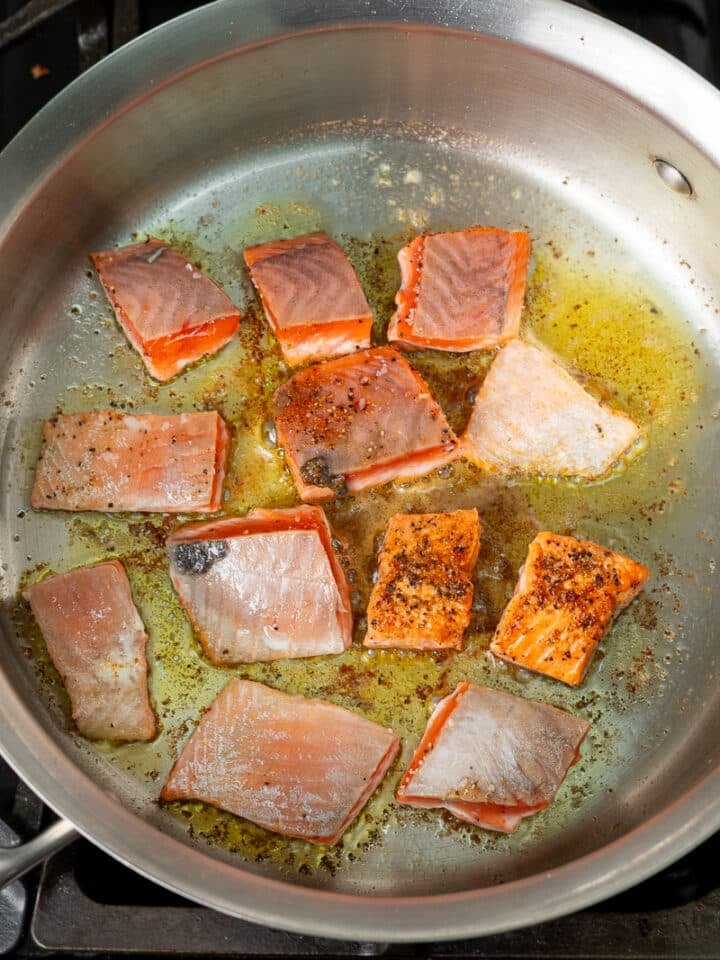 pieces of salmon being seared in a stainless steel skillet