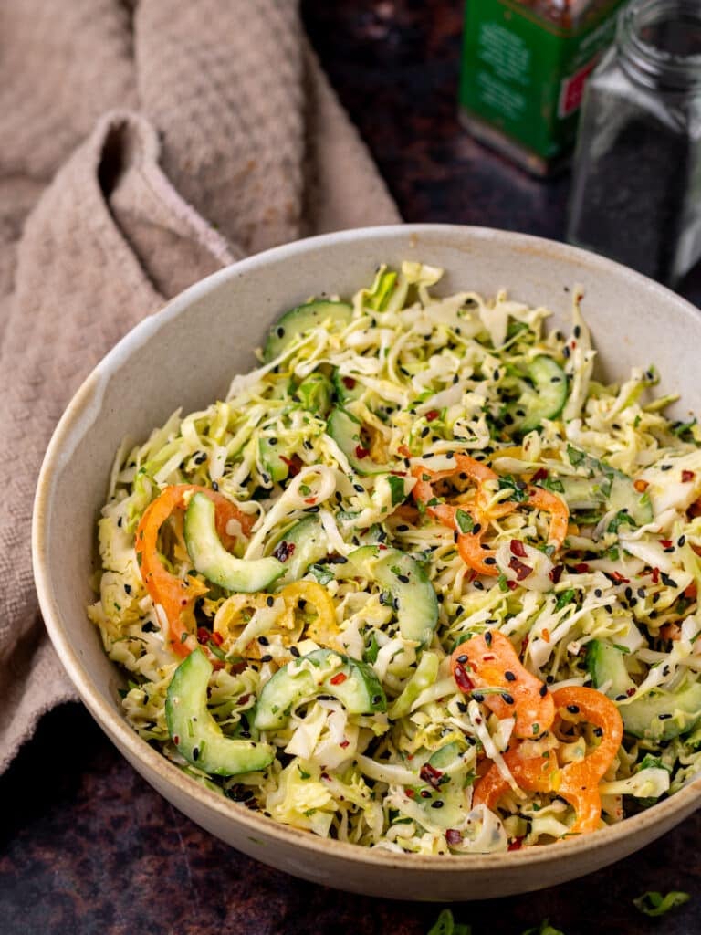 Large bowl of slaw with thinly sliced cucumber, peppers, cabbage, sesame seeds and creamy sweet chili dressing