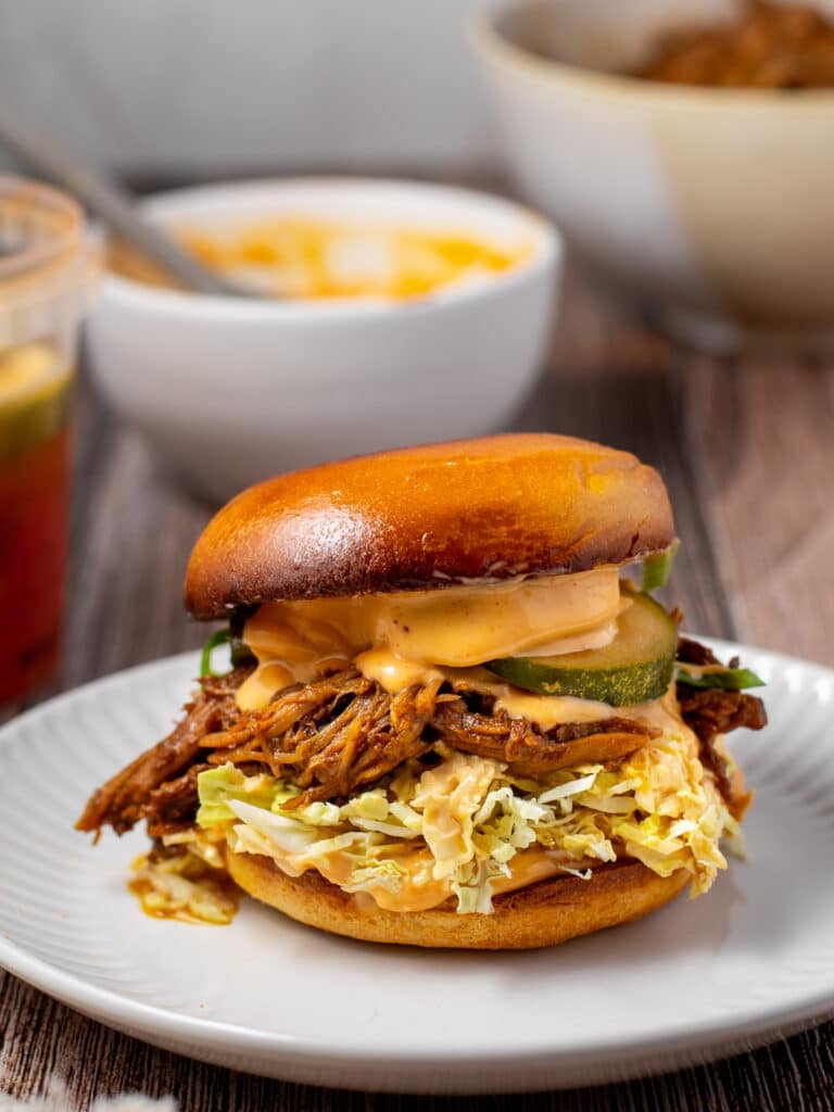 white plate with korean pulled pork sandwich with slaw, kimchi pickles and gochujang aioli
