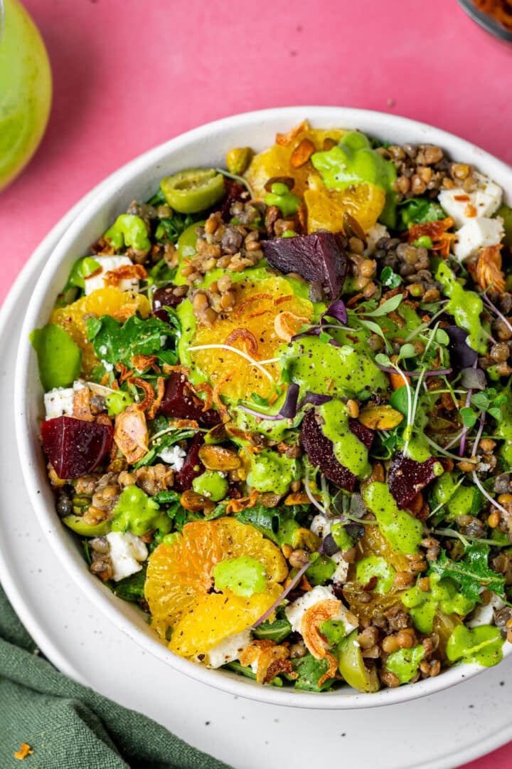 white bowl with arugula, lentils, beets, mandarin oranges, feta, pistachios, shallots and parsley vinaigrette