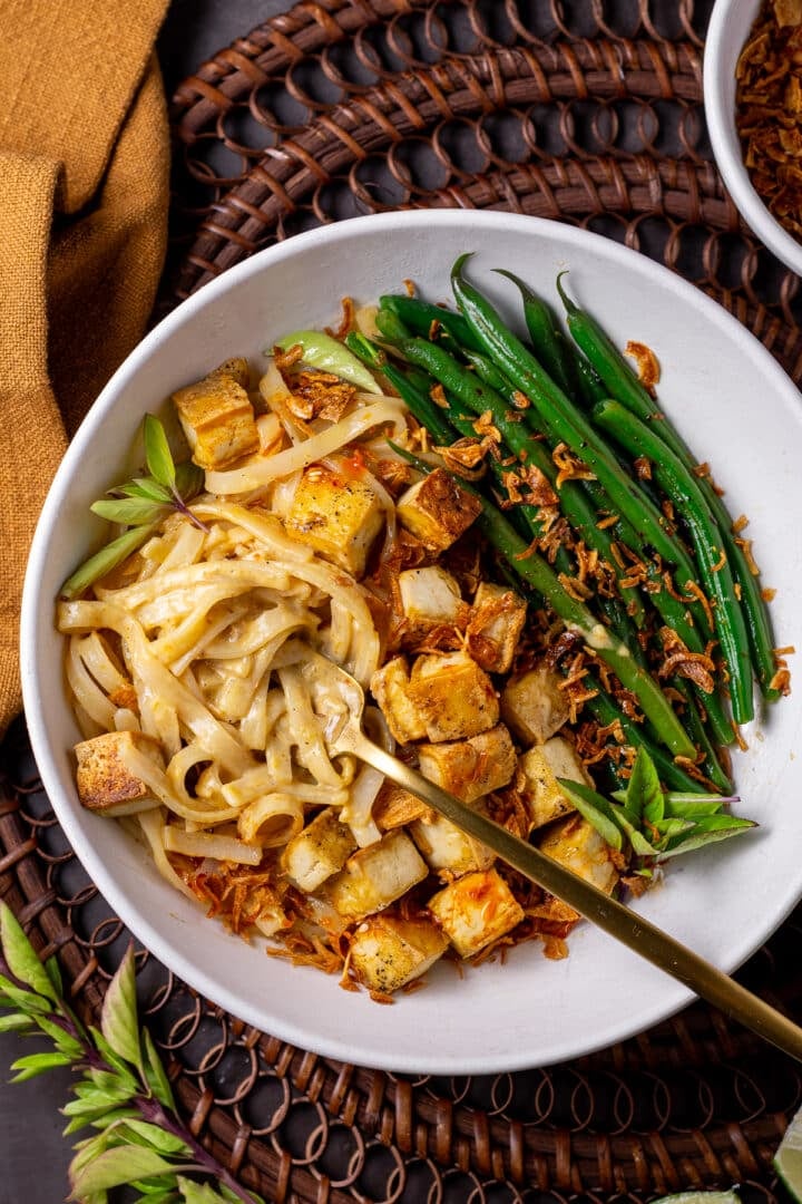 shallow bowl with a fork twisting curry noodles, topped with crispy tofu and chili crunch green beans