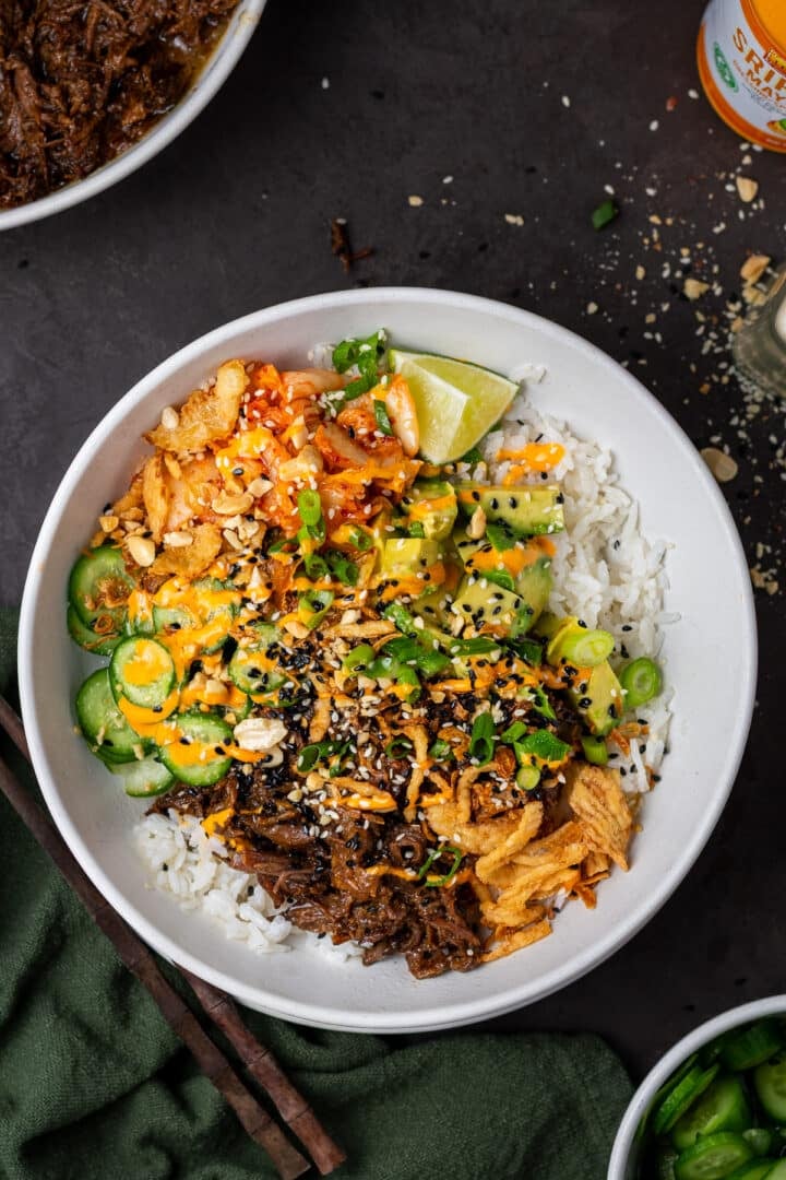 rice bowl with beef, cucumbers, crispy fried onions, green onions, kimchi and sriracha mayo