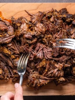 two forks shredding beef on a cutting board