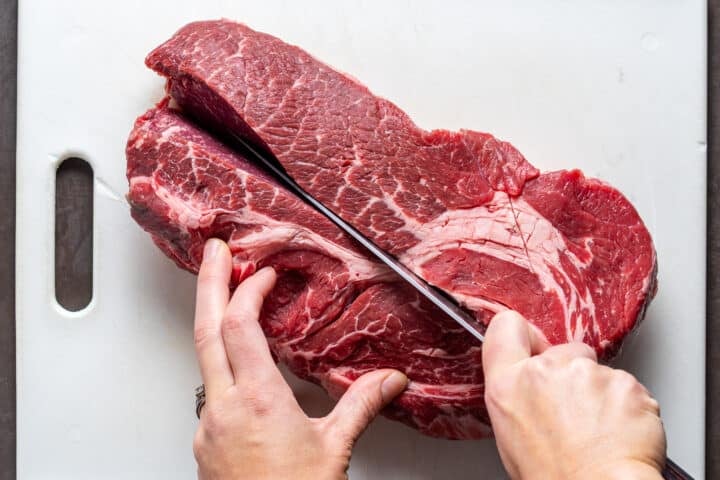 hands using a chef knife to slice a beef chuck roast