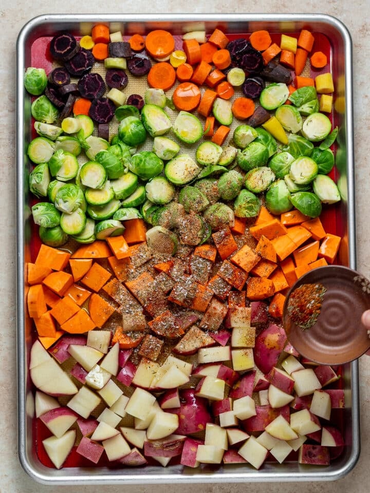seasonings and olive oil added to veggies on a sheet pan