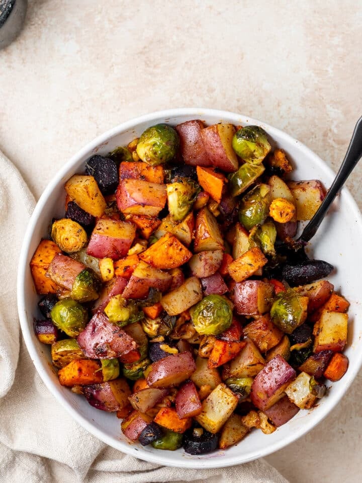 white serving bowl with honey roasted sweet potatoes, red potatoes, brussels sprouts and carrots