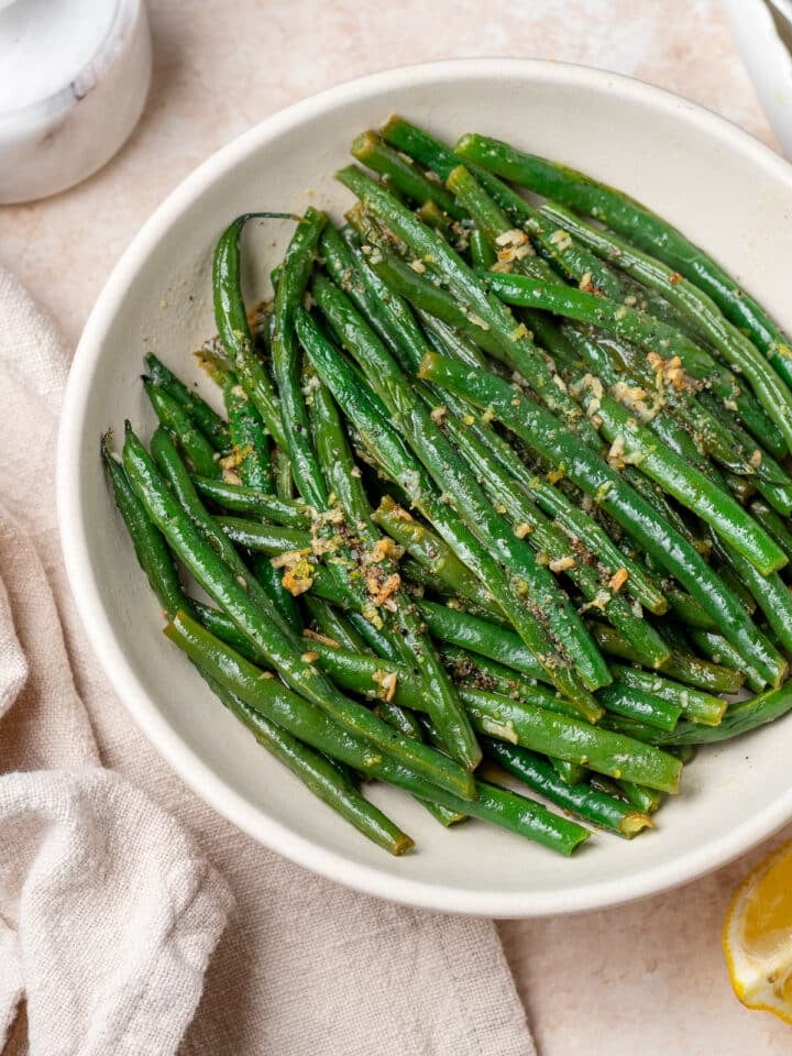 white bowl with cooked green beans specked with lemon zest and minced garlic