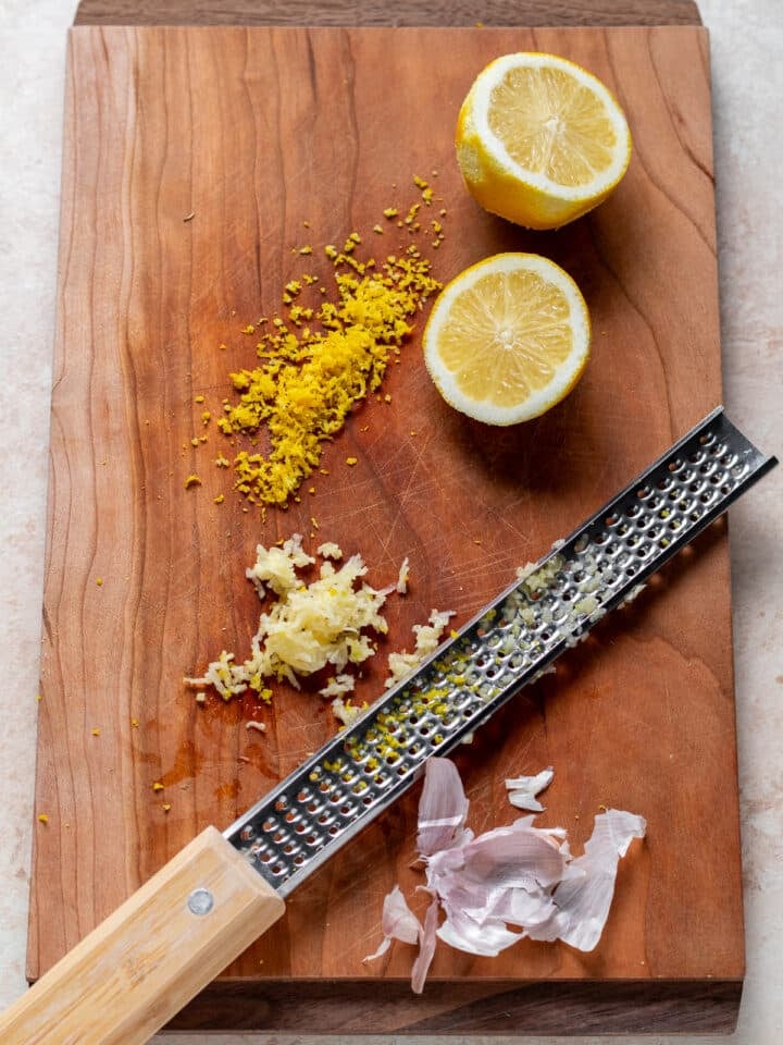 wood cutting board with lemon zest, minced garlic and a microplane