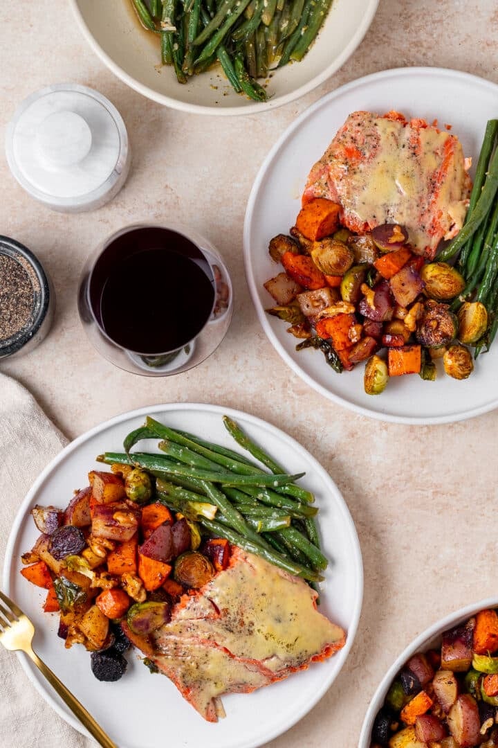 two white plates filled with salmon, roasted vegetables and green beans