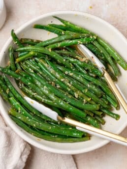white bowl with lemon butter green beans and white tongs