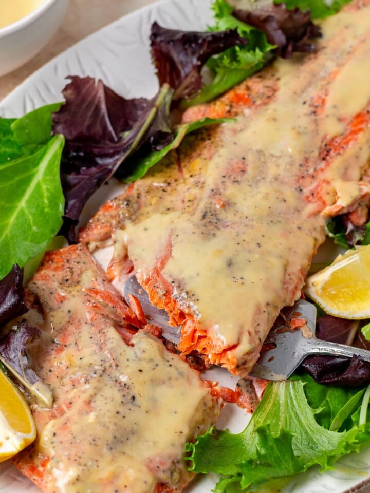 salmon with maple mustard glaze on a large white platter with greens and lemon wedges