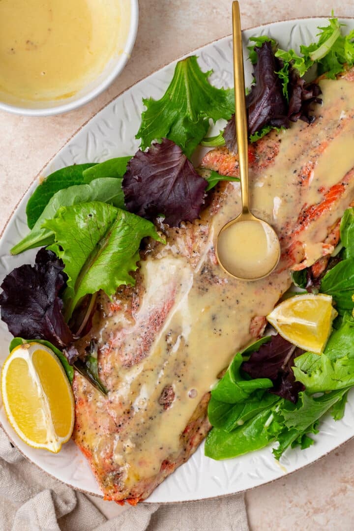 salmon on a white platter with a gold spoon drizzling extra sauce over the cooked fillet