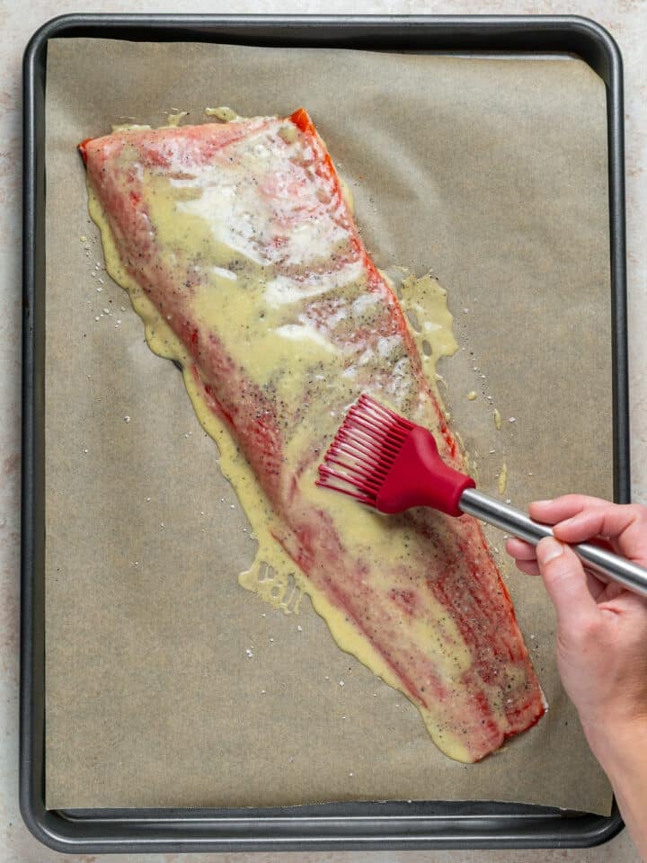 using a pastry brush to brush the maple dijon glaze on the salmon