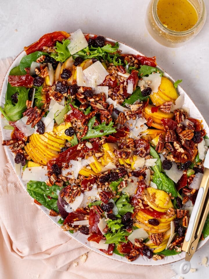 overhead view of a pear and pecan salad with crispy prosciutto, parmesan cheese and dried cherries