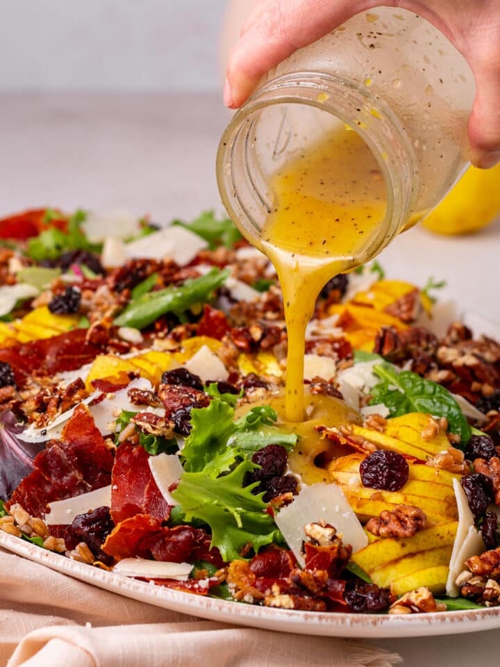 pouring honey lemon dressing on a pear and pecan salad