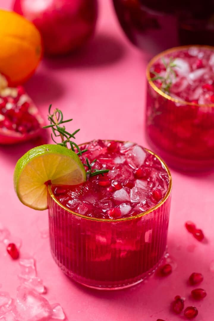 close up view of a glass with sparkly pomegranate punch, garnished with a sprig of rosemary and lime slice