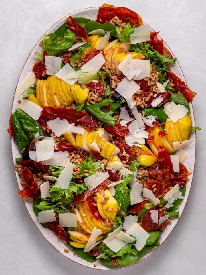 large salad platter with mixed greens, pears, farro, prosciutto and parmesan shards