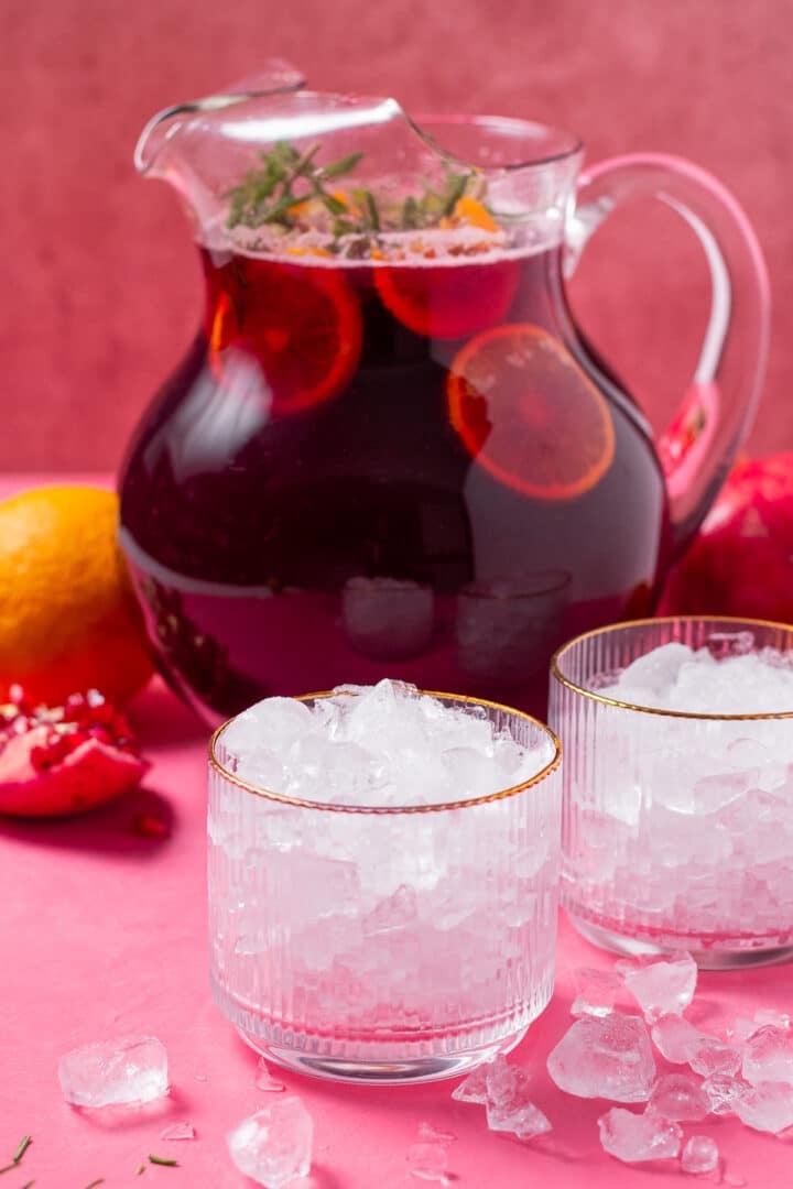 two glasses with crushed ice, pitcher of pomegranate punch with fruit slices