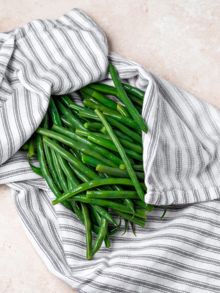 cooked green beans being patted dry with a gray striped kitchen towel