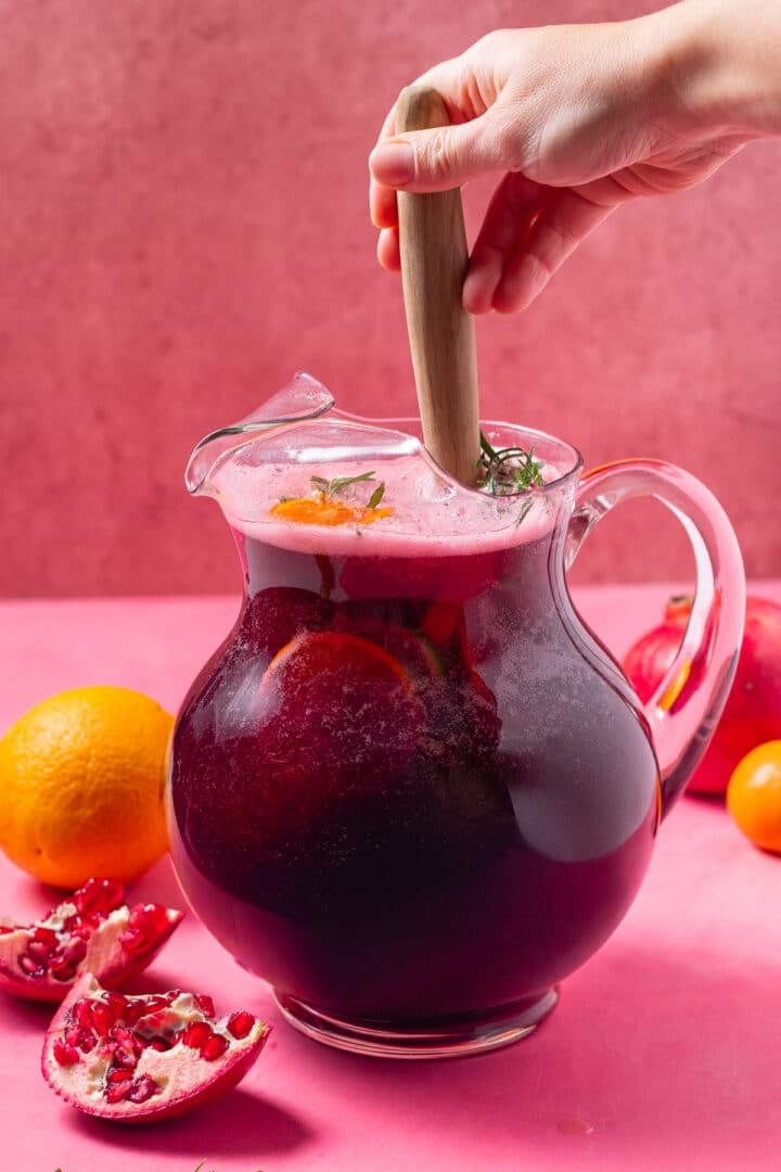 hand using a wooden spoon to stir the pitcher of pomegranate punch