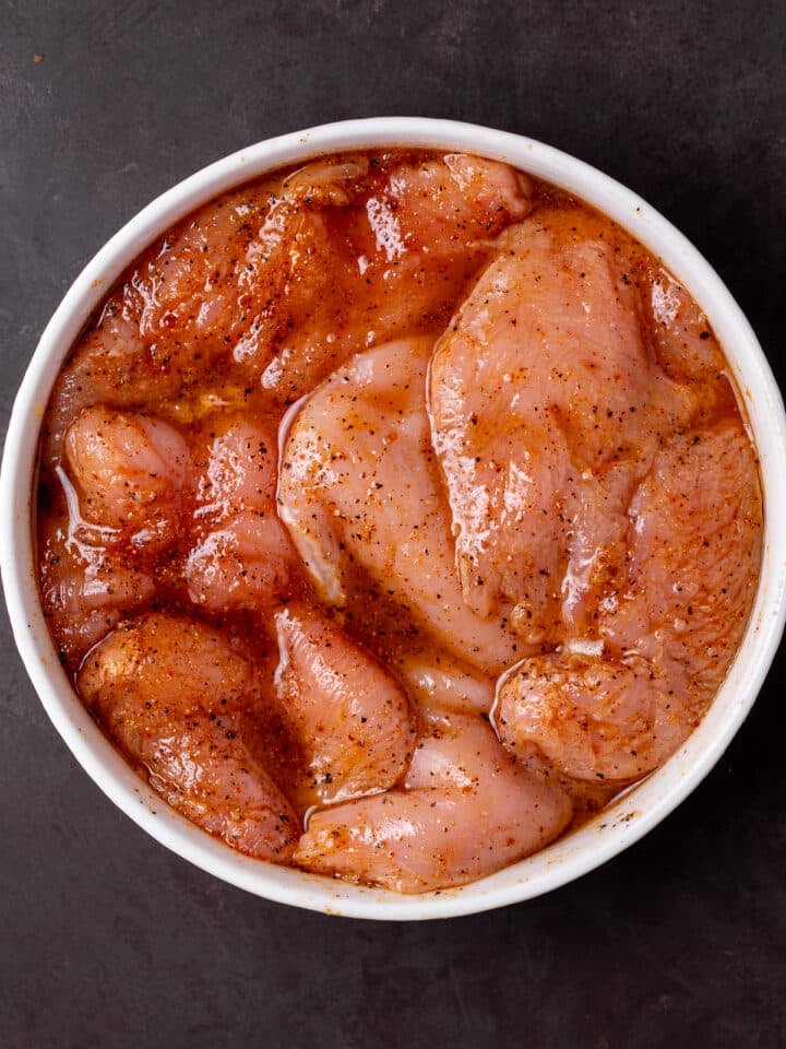chicken marinating in a white bowl