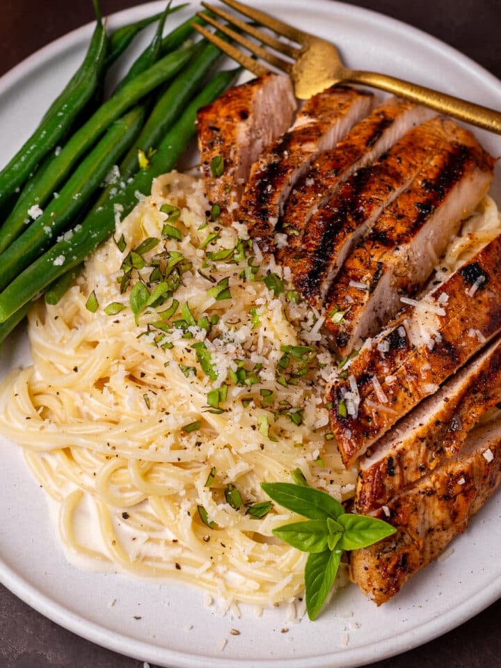 creamy spaghetti alfredo on a plate with seasoned chicken, basil and green beans