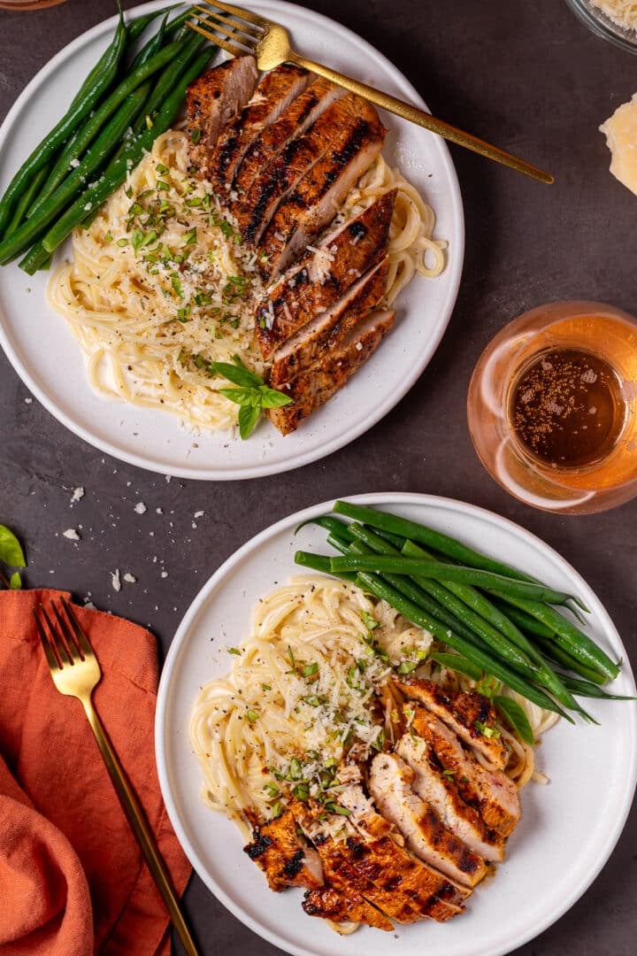 two plates of spaghetti alfredo with grilled chicken, paired with green beans, glass of rosé