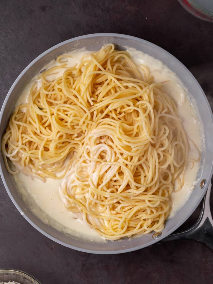 drained spaghetti noodles added to the alfredo sauce in the skillet