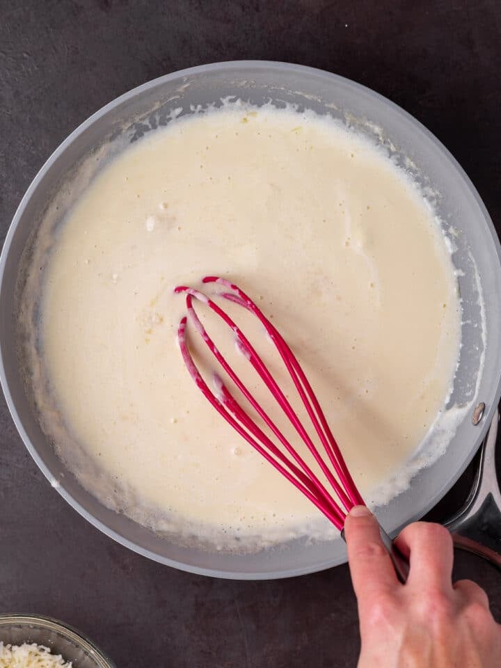 hand using a whisk to whisk together the alfredo sauce