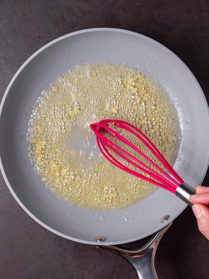 pink silicone whisk whisking the melted butter and garlic
