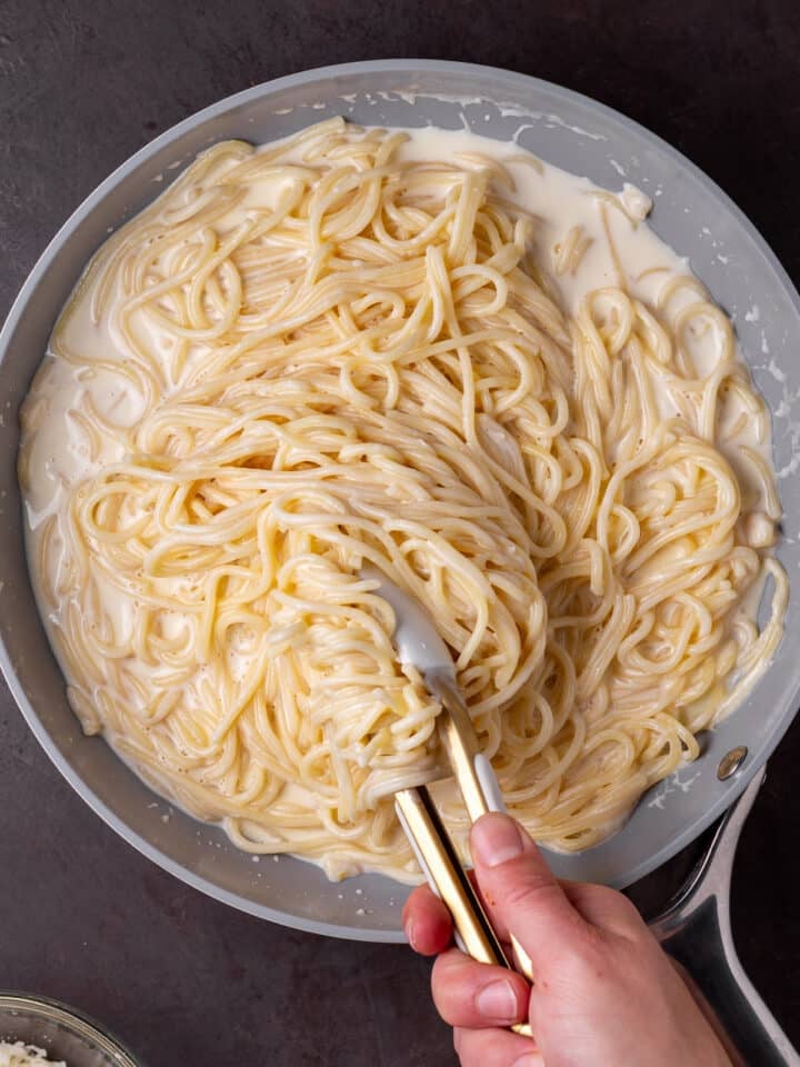 using tongs to toss cooked spaghetti with sauce