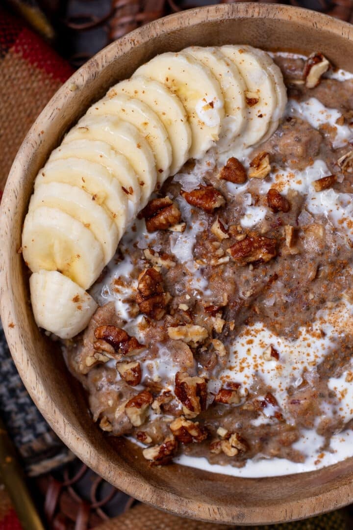close up view of sticky date oatmeal topped with pecans, banana slices and a drizzle of cream