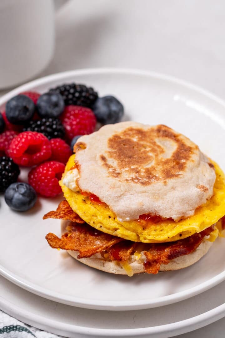 high protein breakfast sandwich with egg and cottage cheese, bacon, cheese, fresh berries on the side