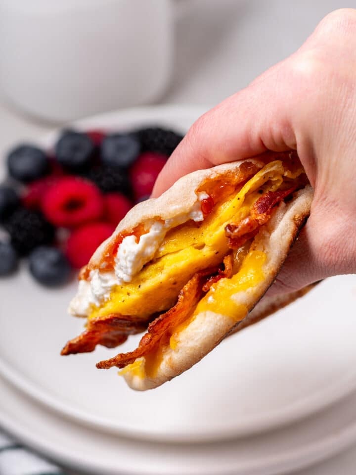 hand holding a breakfast sandwich with egg, bacon, cheese and pepper jelly