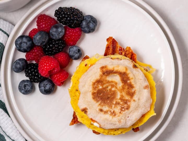 overhead shot of a high protein breakfast sandwich on a white plate with some fresh berries