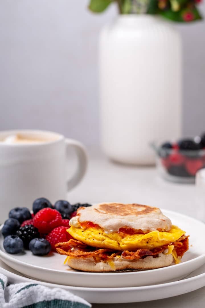 high protein breakfast sandwich with egg, bacon and pepper jelly, mug of coffee, fresh berries