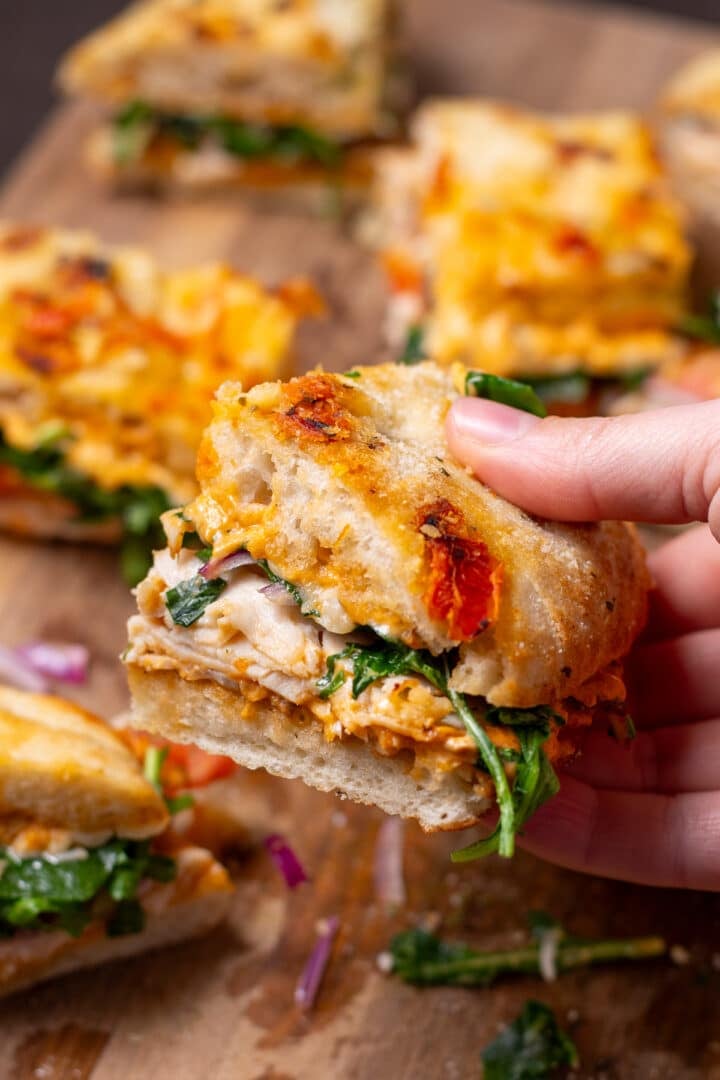 hand holding a sandwich made on focaccia bread with chicken, arugula, pesto mayo and red onion