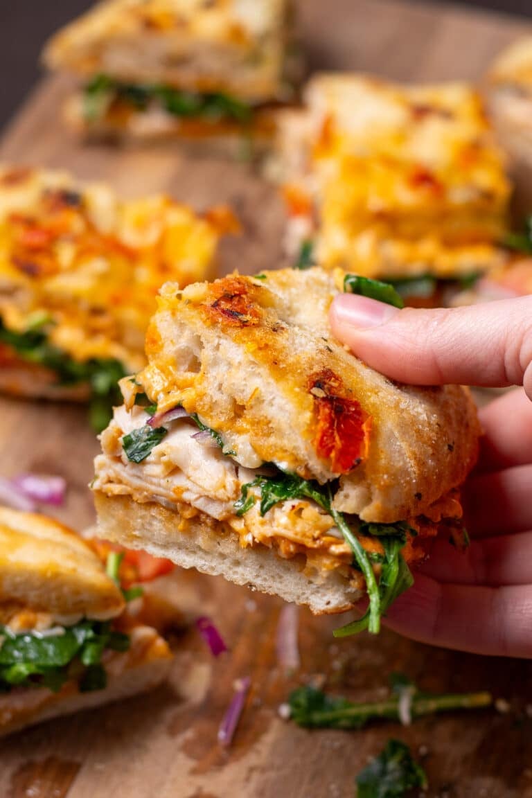hand holding a sandwich made on focaccia bread with chicken, arugula, pesto mayo and red onion