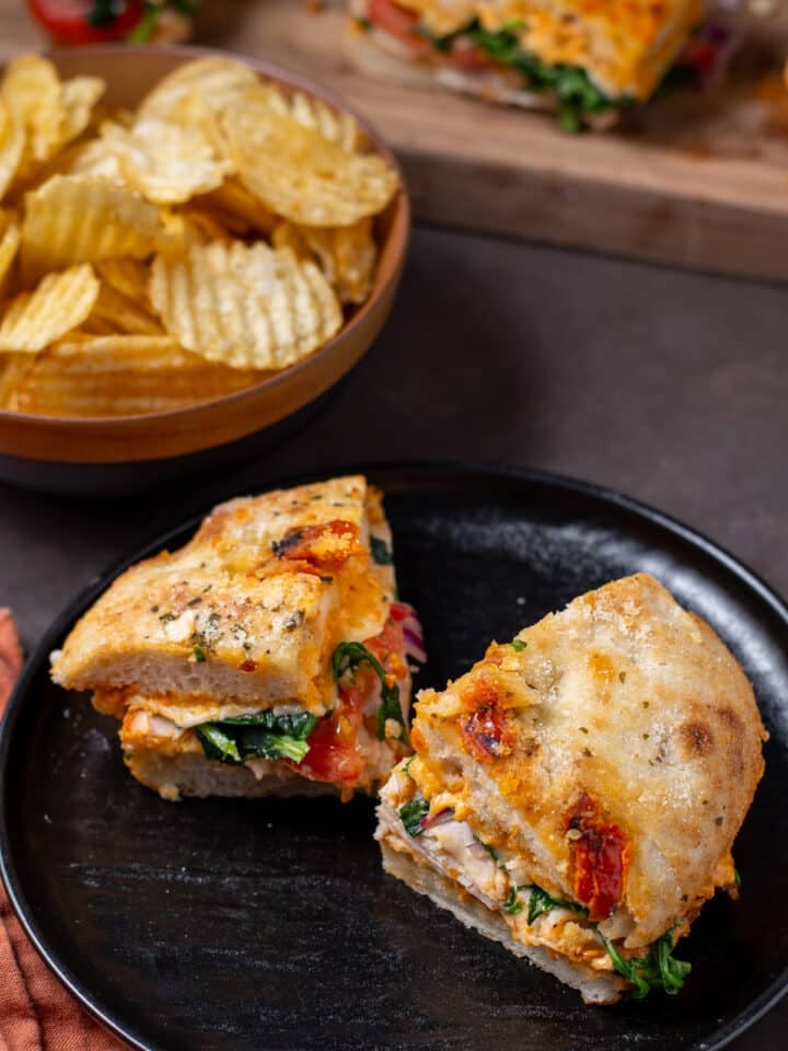 two pieces of sandwich on a black plate, bowl of potato chips