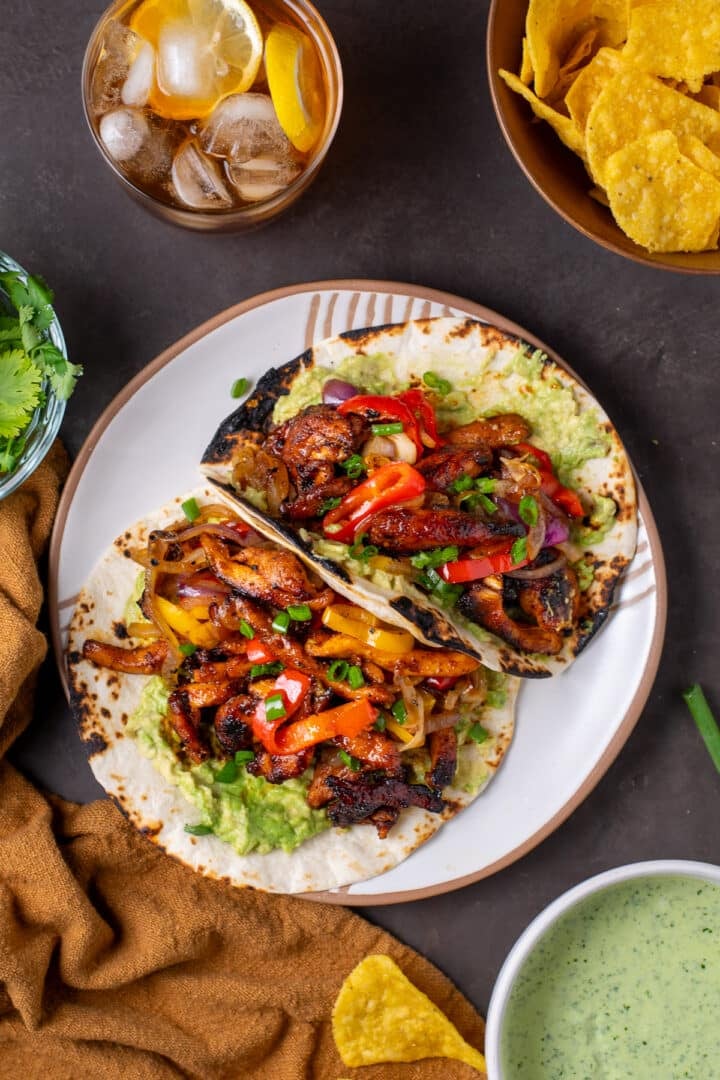 white plate with two fajitas filled with chipotle chicken, sauteed veggies, guacamole