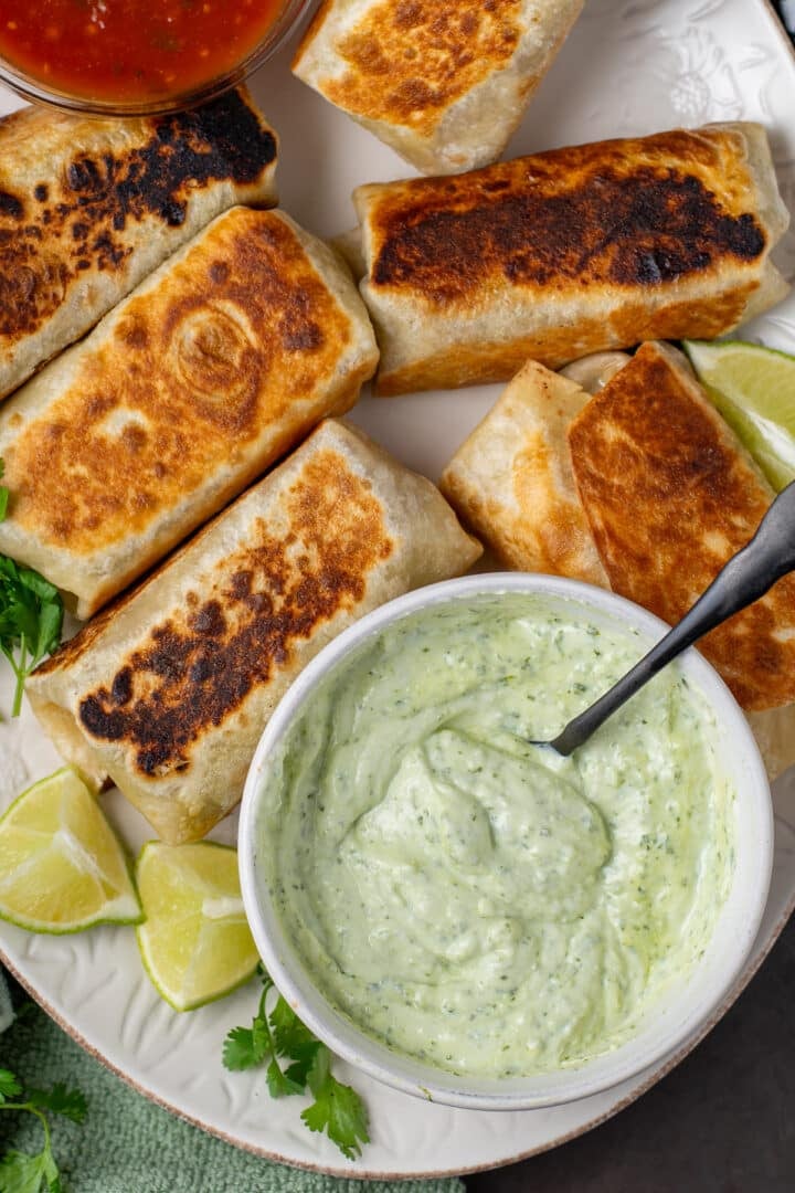 cilantro yogurt sauce in a bowl on a platter with toasted burritos
