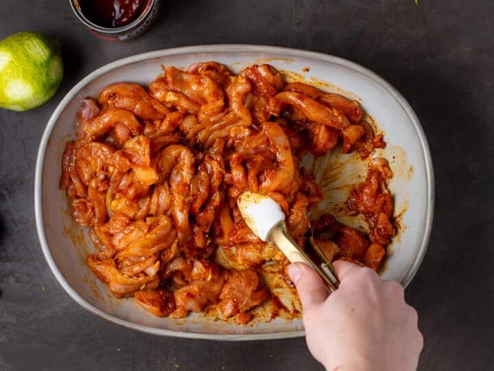 hand using tongs to toss chicken in marinade