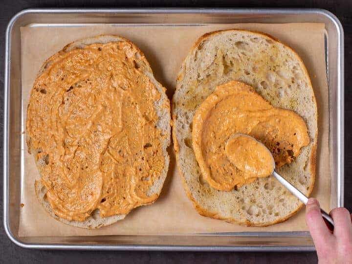 hand spreading pesto mayo on both halves of the focaccia loaf