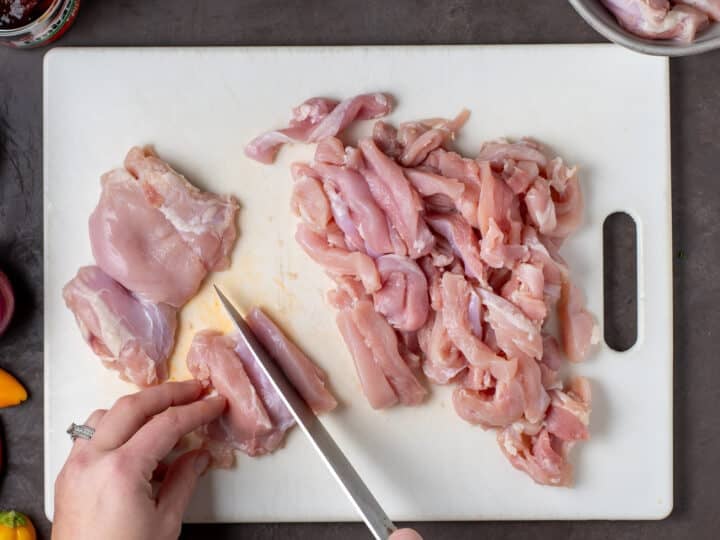 hands using a knife to slice chicken thighs