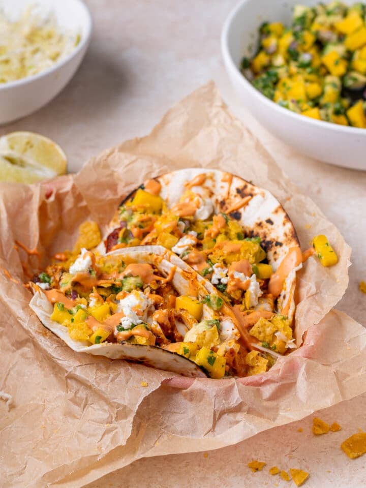 basked with parchment paper and two fish tacos with mango pico, cheese and chipotle aioli