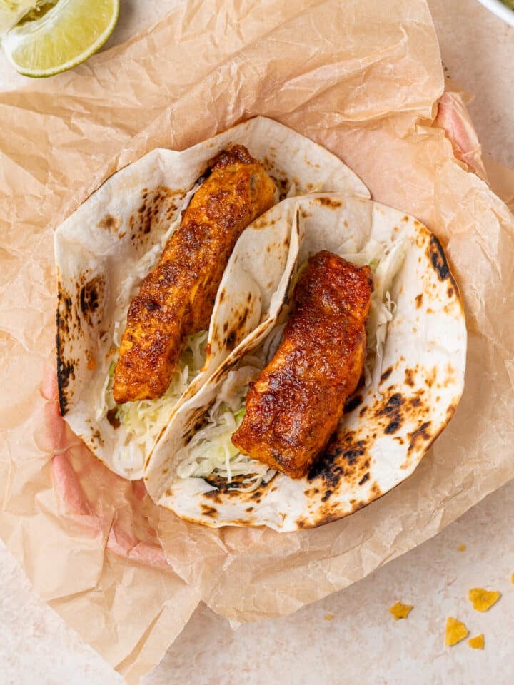 two flour tortillas filled with cabbage and seasoned white fish